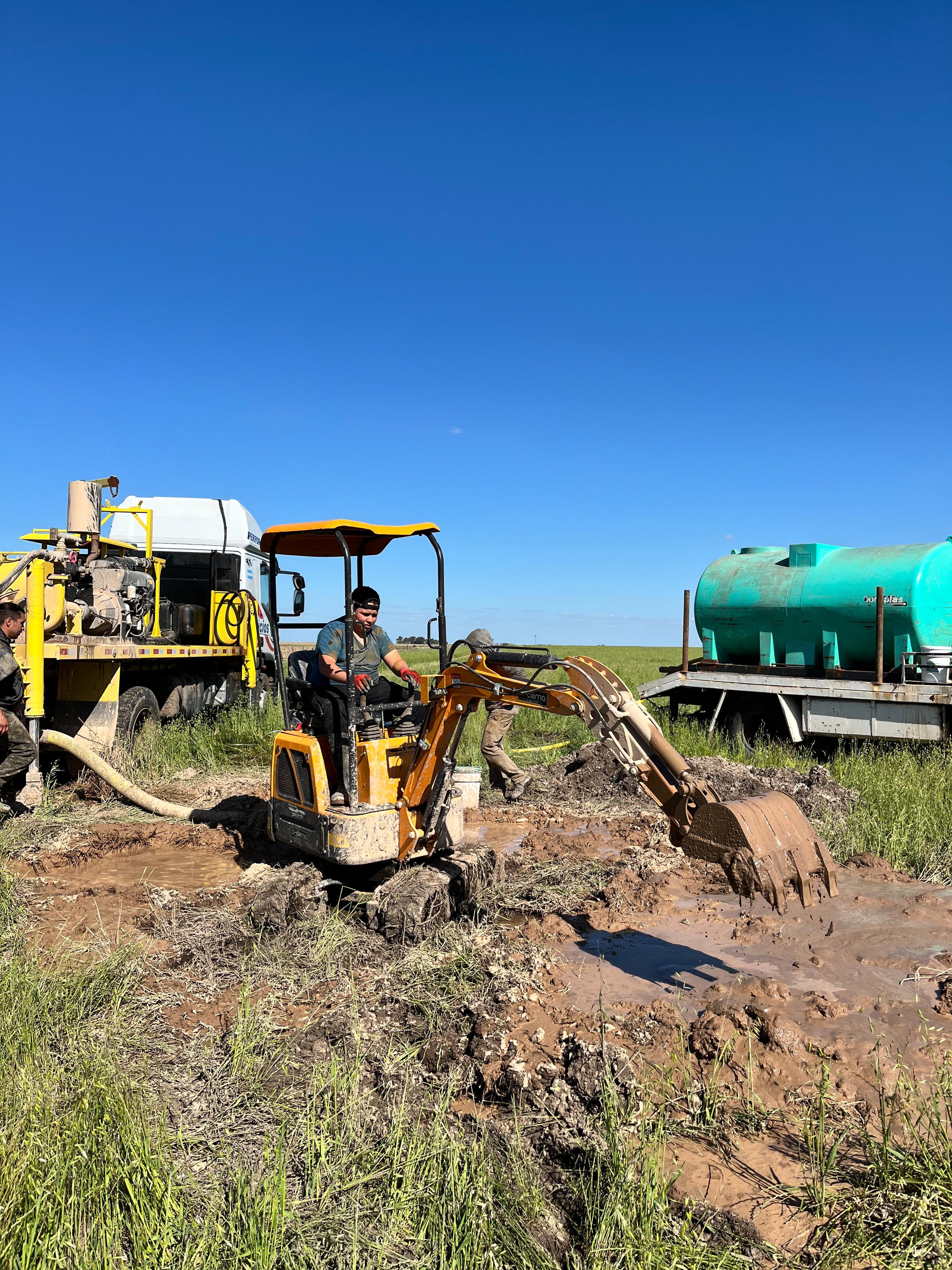 Mini excavadora abriendo una calicata junto a un camión cisterna
